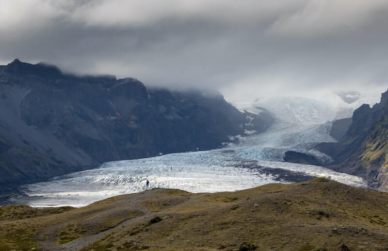 霧の中、緑の苔山から流れ落ちるアイスランドのエイヤフィヤラヨークトル氷河